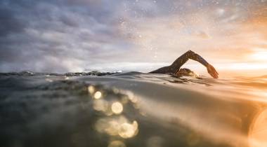 persona che nuota in acque libere al tramonto